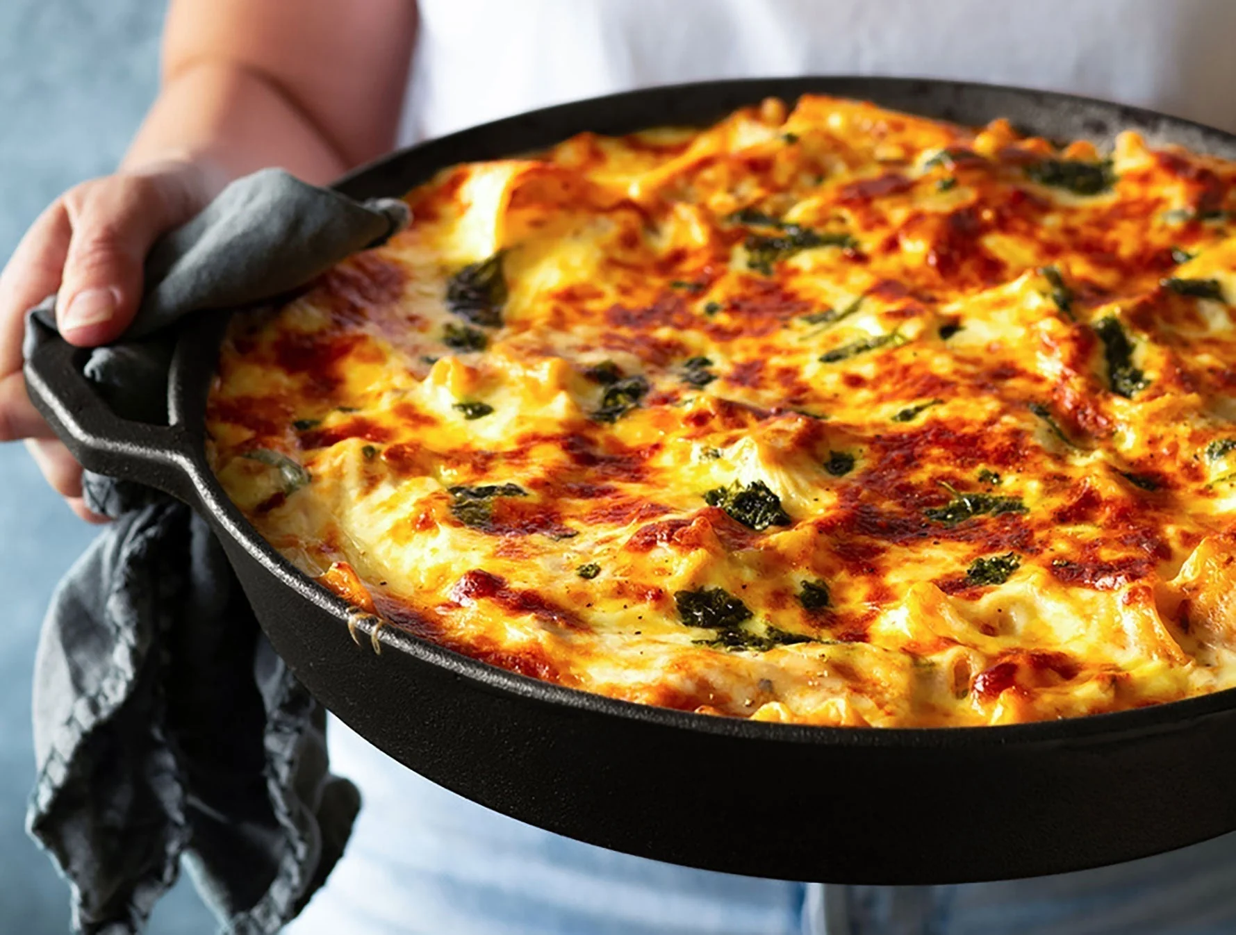 Hands in an oven mitt holding a cast iron skillet of baked eggs